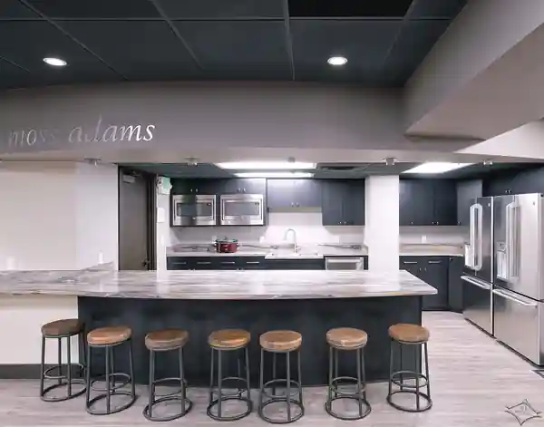 Commercial office break room with a long counter, stools and dark ceiling designed for Moss Adams
