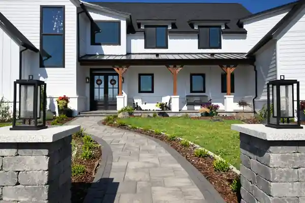 White farmhouse-style new home with lantern-topped stone pillars from the 2023 Tour of Homes